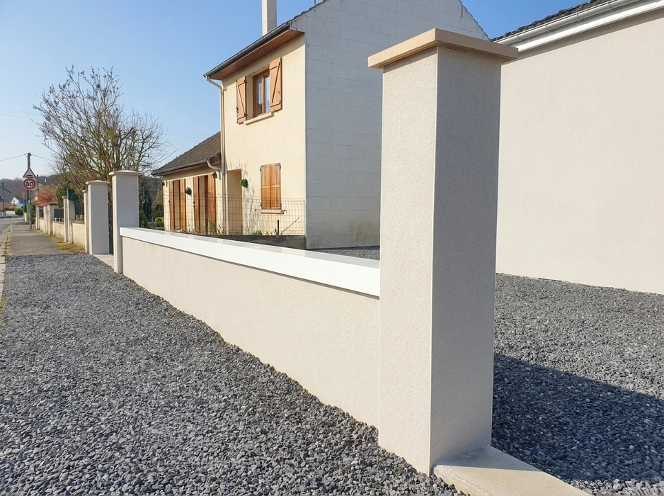 Clôture en maçonnerie enduite ton beige-blanc, composée de piliers carrés et d'un muret bas avec chaperon plat