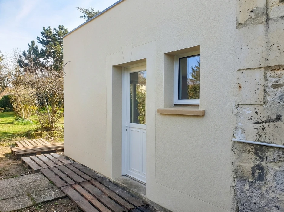 Extension de maison moderne avec façade enduit blanc cassé, porte d'entrée PVC blanche vitrée mi-hauteur et fenêtre PVC double vitrage avec appui de fenêtre en pierre reconstituée