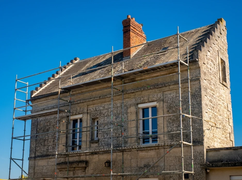Façade en pierre calcaire d'un bâtiment ancien en rénovation, avec échafaudage tubulaire métallique multi-niveaux