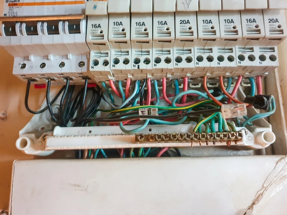 Électricien ou technicien expérimenté inspectant visuellement un tableau électrique mural, utilisant un multimètre ou un équipement de diagnostic pour tester les connexions. L'électricien porte des équipements de sécurité appropriés. L'image montre un intérieur résidentiel avec un tableau électrique clairement visible, mettant en évidence l'aspect technique et sérieux de la mise en conformité électrique d'un logement.