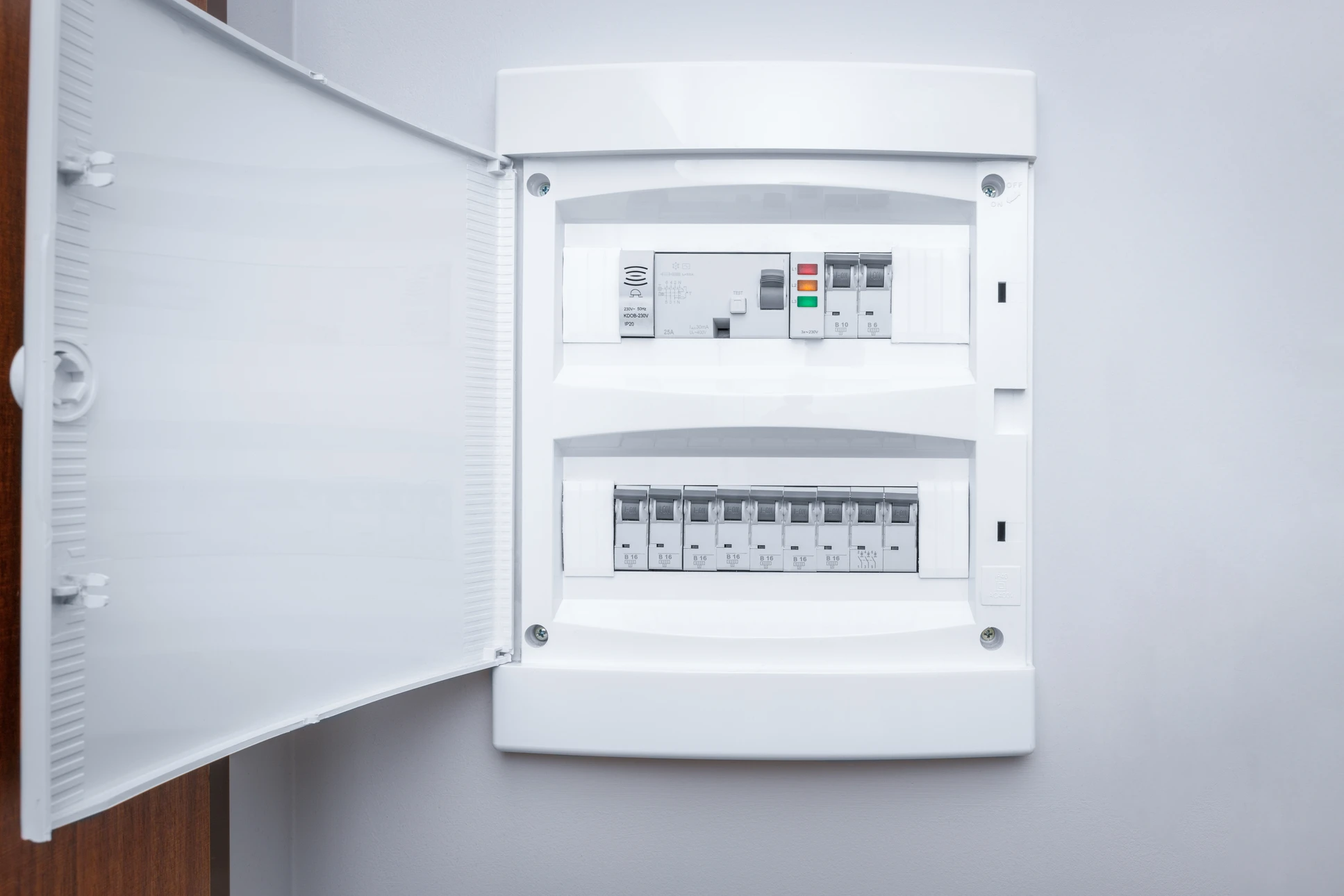 Électricien effectuant des mesures dans un tableau électrique résidentiel, tenant un multimètre numérique orange affichant 18